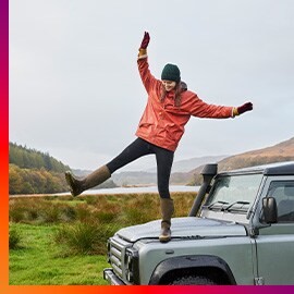 Woman balancing on one leg on hood of rugged SUV next to lake