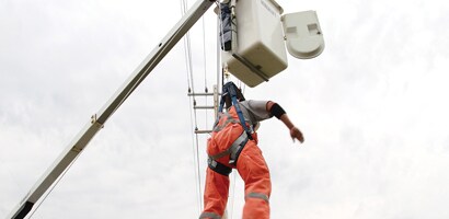 Worker suspended below cherry picker from fall protection system 
