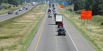 A highway work zone with traffic passing by orange road construction signs.
