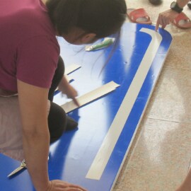 A person kneels over a reflective road sign during the sign-fabrication process.