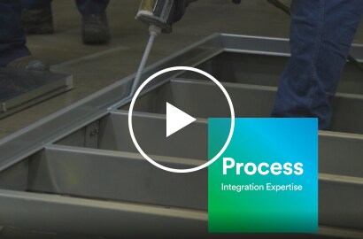 Video still of liquid adhesive application to a frame before adding a panel, with text “Process – Integration Expertise”