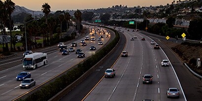 A busy eight-lane highway at dusk has easily viewable pavement markings.
