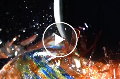 Video still of a weight smashing a glass ball after mechanical fasteners failed to hold metal panels together to protect it.