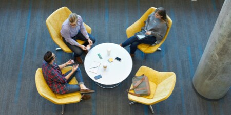 Overhead view of three people sitting in chairs at a small round table having a discussion.
