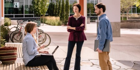 Three people on a corporate campus talking to each other.
