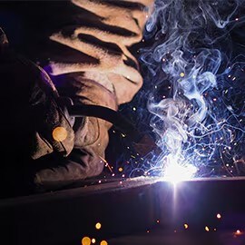 Soldador trabajando, con chispas y humo alrededor.