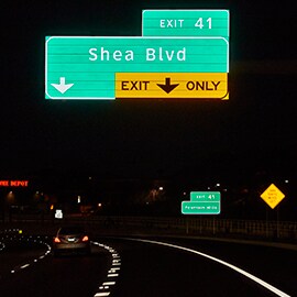 Highway at night with illuminated road sign overhead.