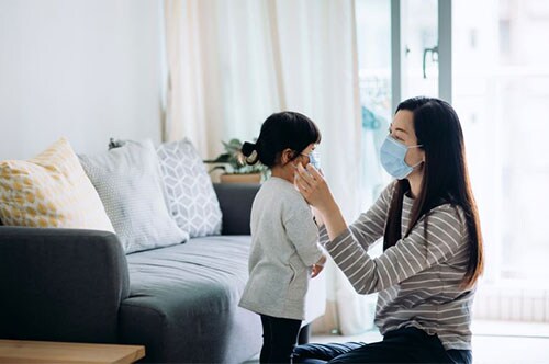 why wearing a mask is important: woman helping young girl put mask on