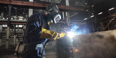 Soldador con equipo de protección que utiliza un soplete de soldadura sobre una estructura metálica en una planta de fabricación.

