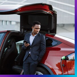 Man on phone standing next to red electric vehicle charging with door open