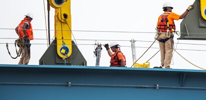 Workers on fall protection gear atop steel beam
